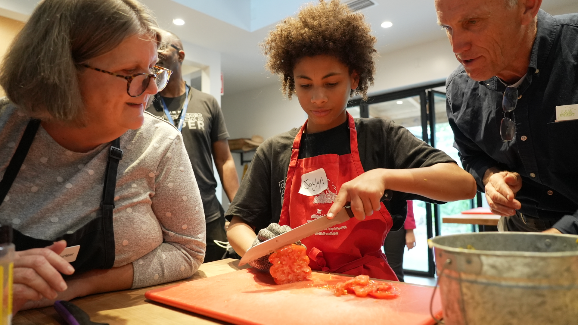 An MBK participant cutting a vegetable during a culinary class with two instructors watching