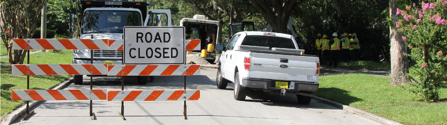 A photo of a road closure sign on a street with a white City of Orlando pick up truck parked near the sign.