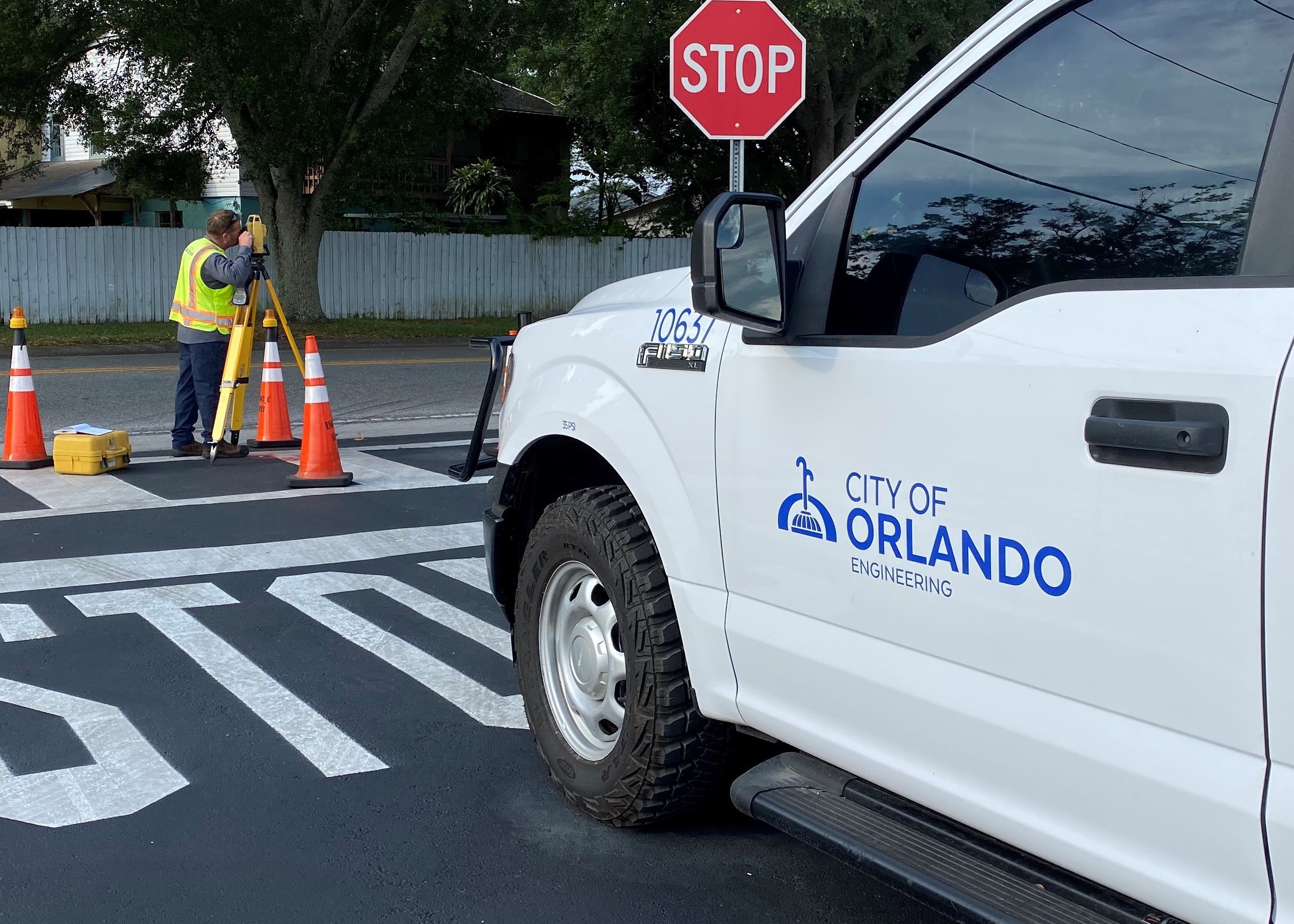 An image of a city employee surveying a city street in front of a white City of Orlando vehicle.