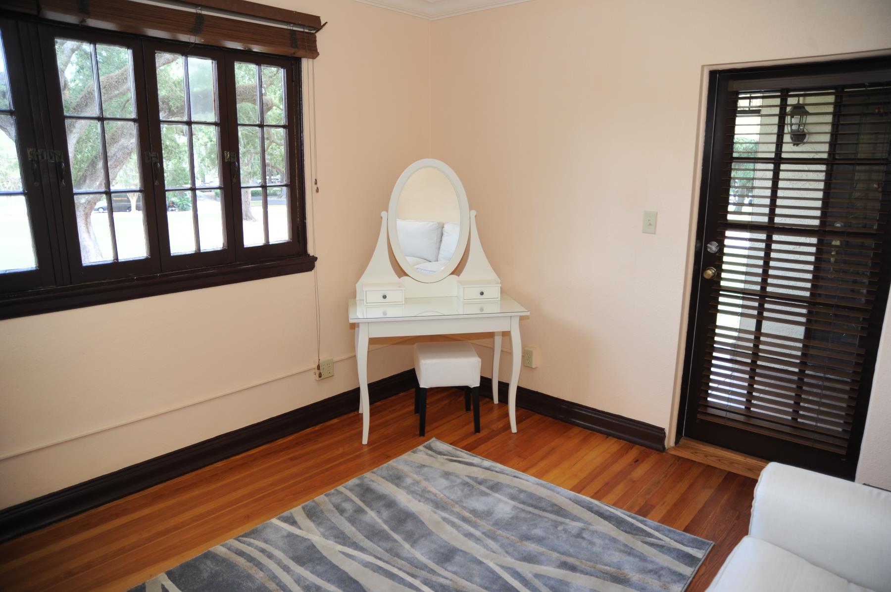 Royal swan room show a vanity in the corner flanked by a row of windows to the left and a door to outside on the right.