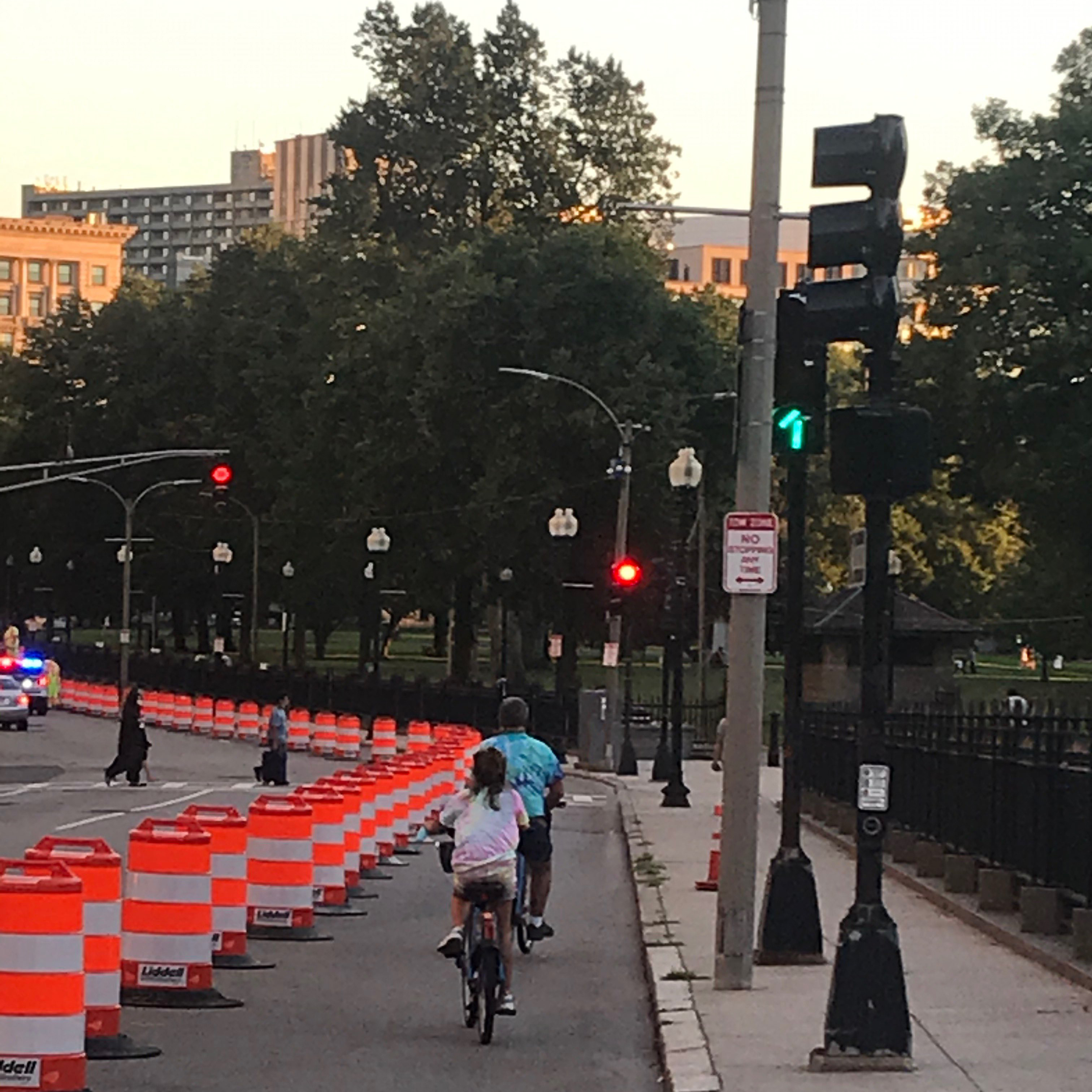 A photograph of people biking along a quick-build bicycle lane delineated by traffic barrels.