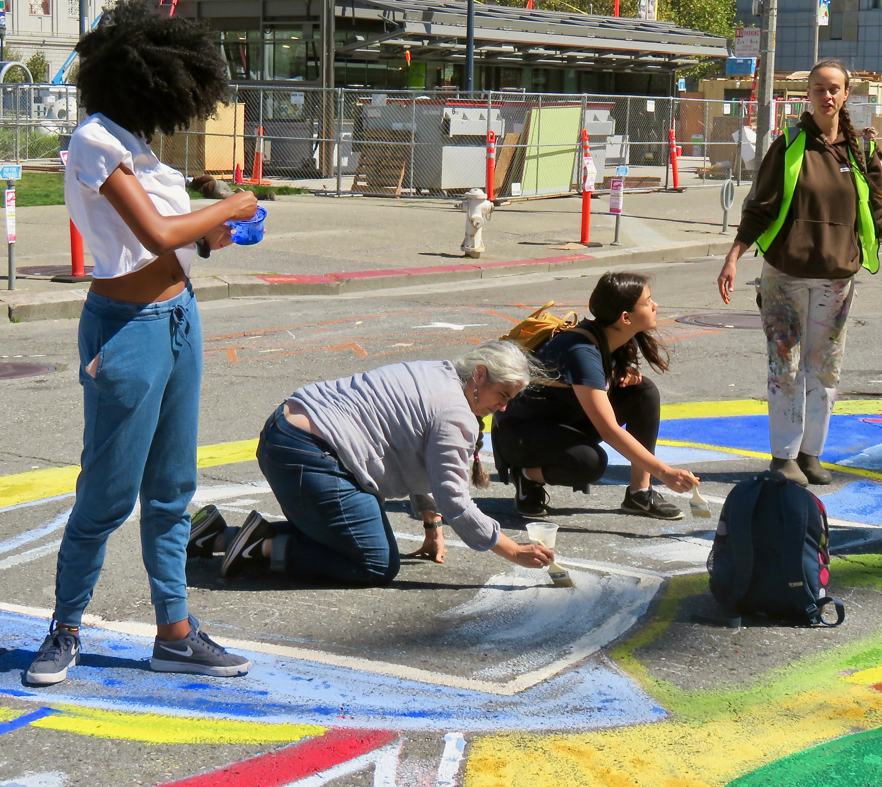 A photograph of volunteers applying tempera paint to an intersection mural in a roadway.