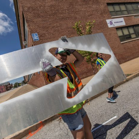 A photo of a person carrying an arrow stencil to be used for marking a quick-build bicycle lane.